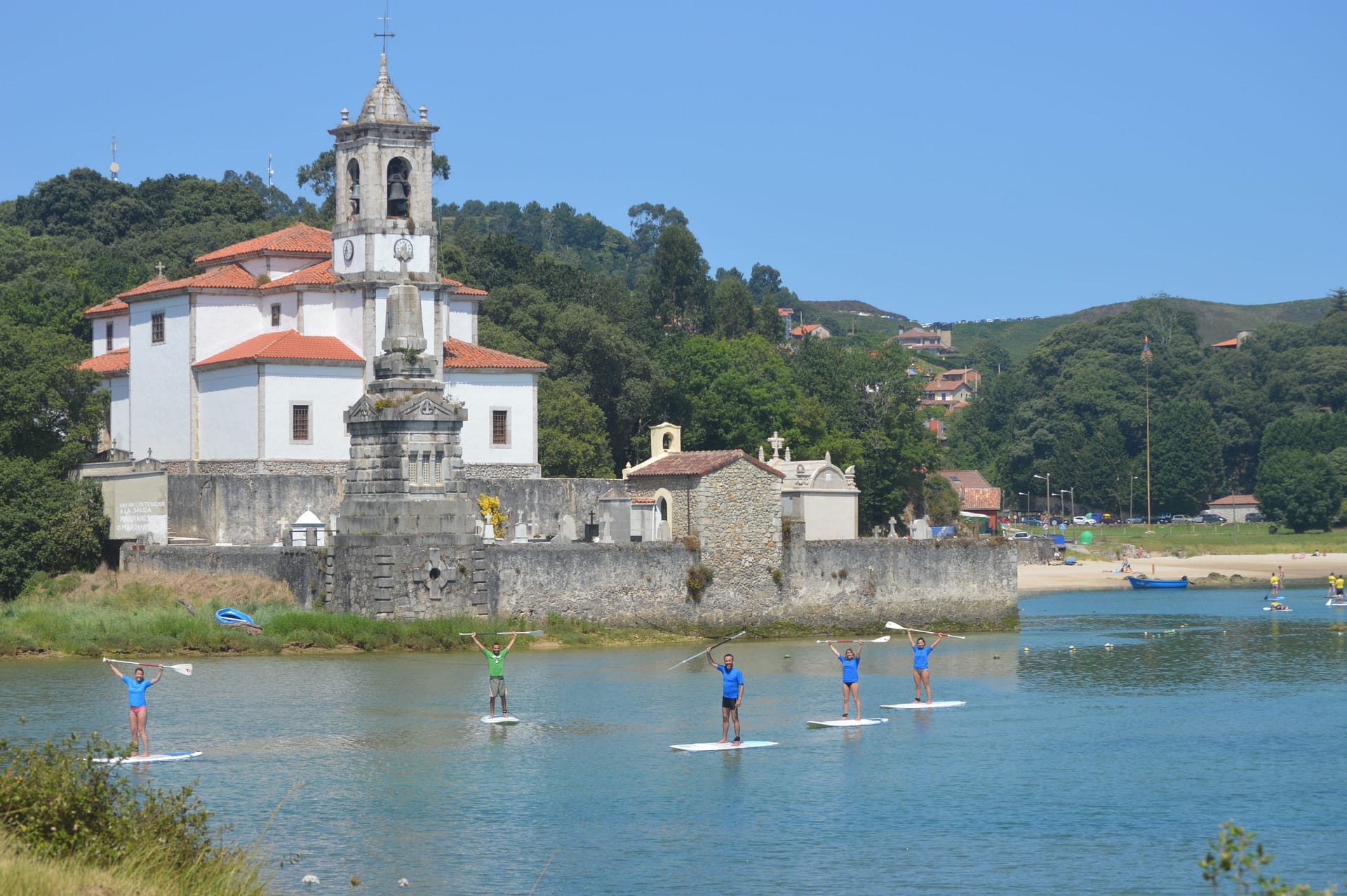 Vista aérea de la Ría de Niembro con practicantes de stand up paddle en el agua turquesa, rodeada de acantilados verdes y montañas de fondo en Llanes, Asturias